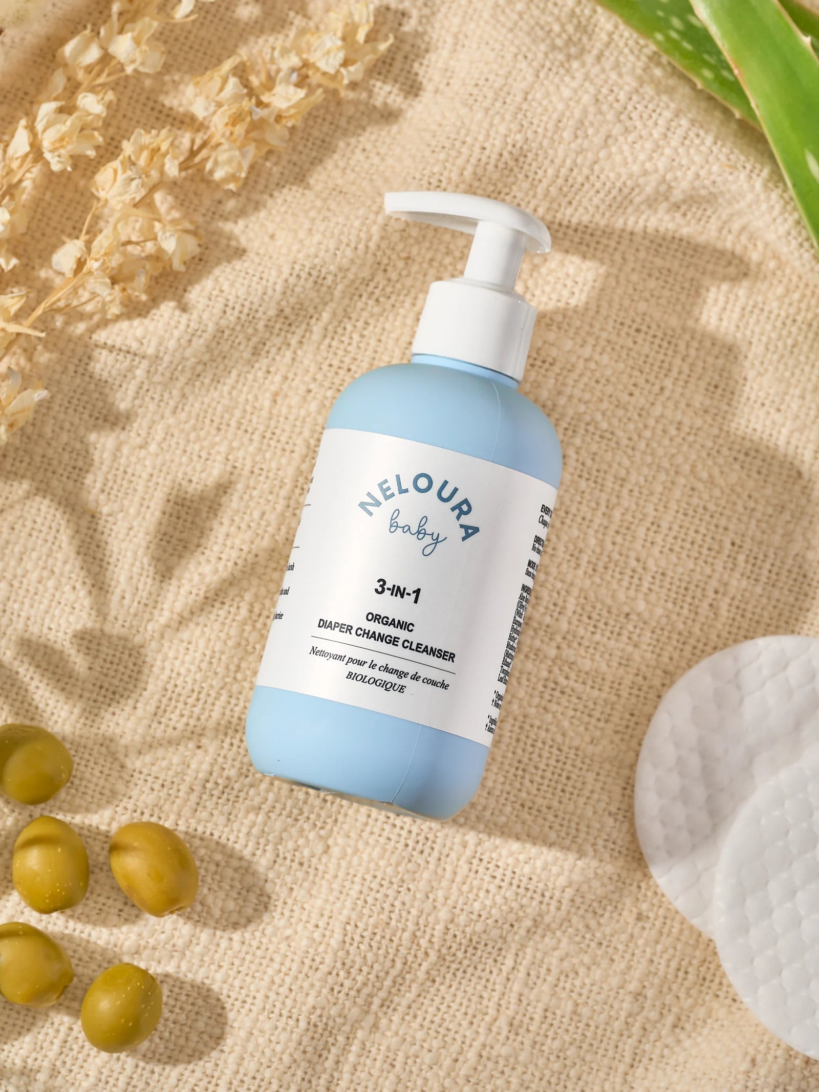 Neloura cleanser on textured linen with cotton pads and olives.